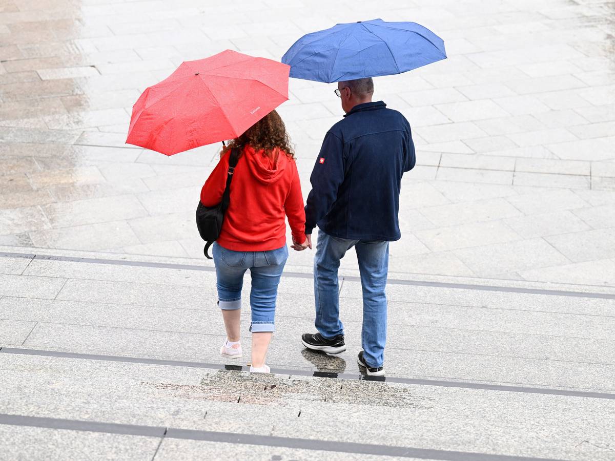 Spaziergänger schützen sich auf dem Bahnhofsvorplatz mit Schirmen vor dem Regen.