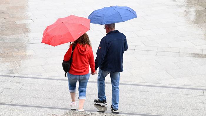 Spaziergänger schützen sich auf dem Bahnhofsvorplatz mit Schirmen vor dem Regen.