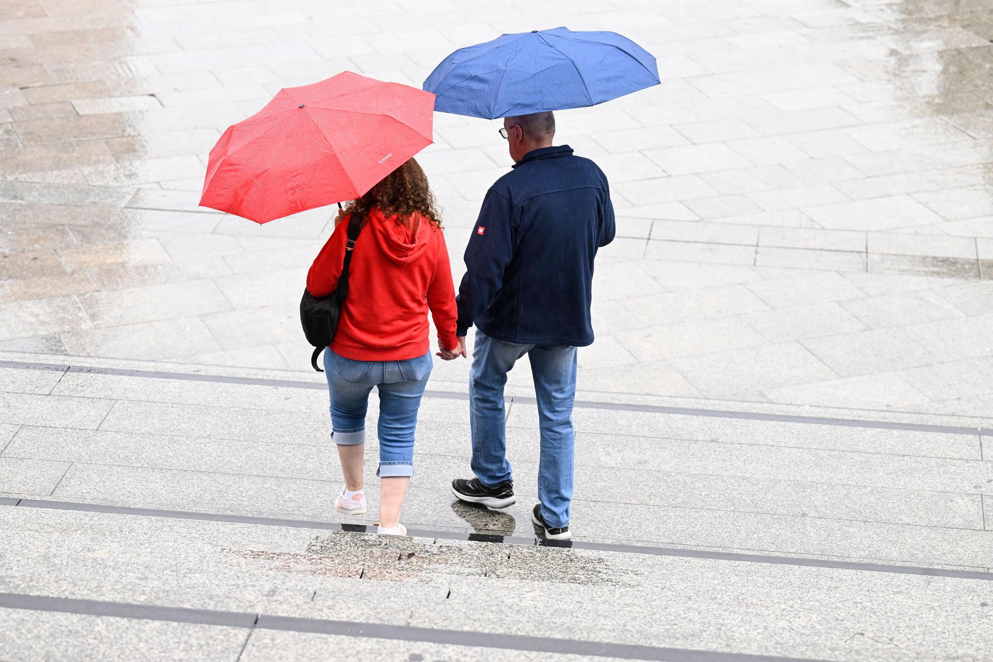 Spaziergänger schützen sich auf dem Bahnhofsvorplatz mit Schirmen vor dem Regen.