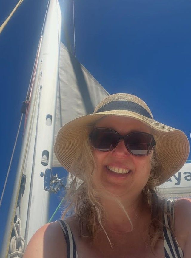Eine Frau mit Strohhut und Sonnenbrille lacht in die Kamera