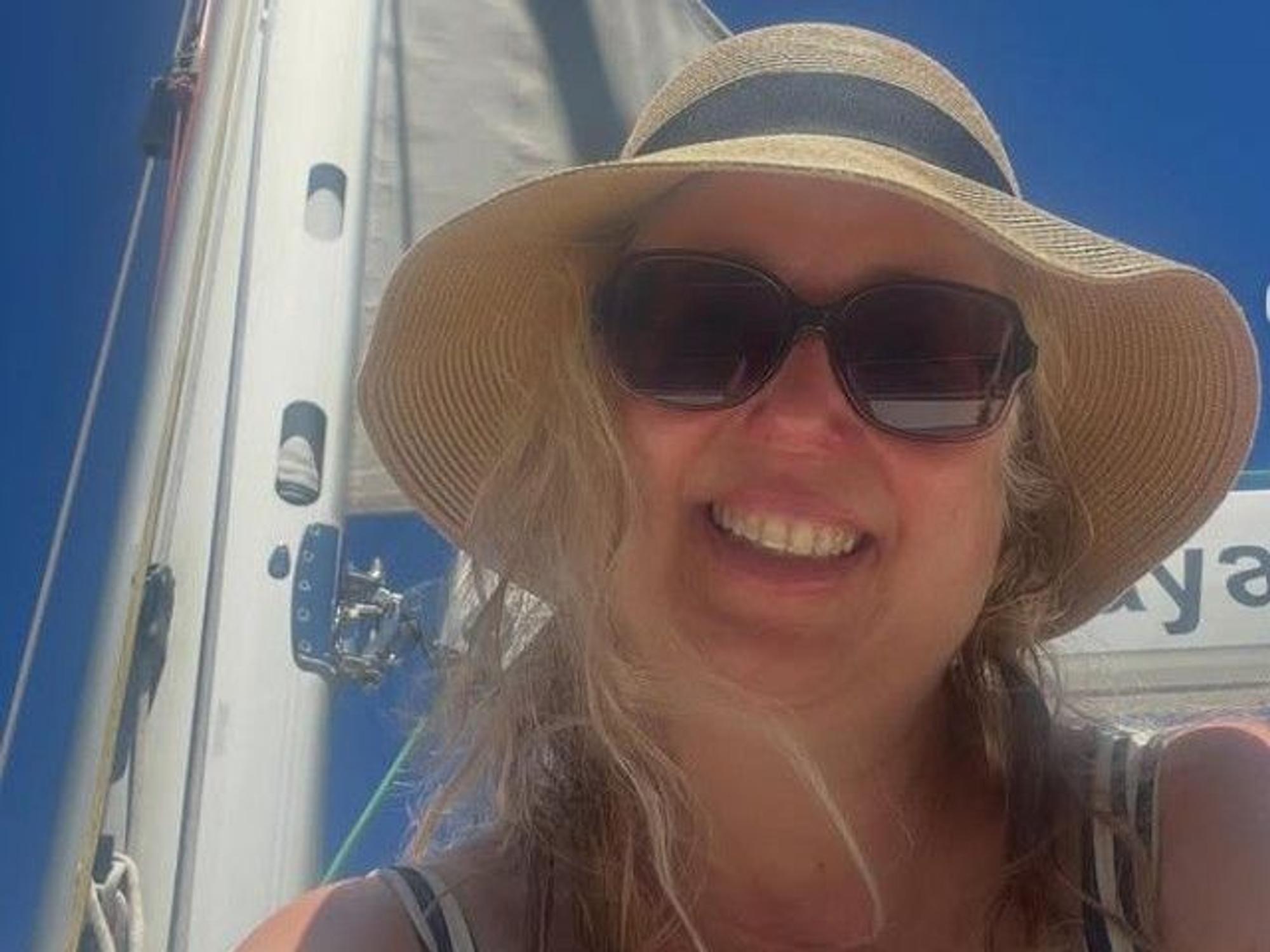 Eine Frau mit Strohhut und Sonnenbrille lacht in die Kamera
