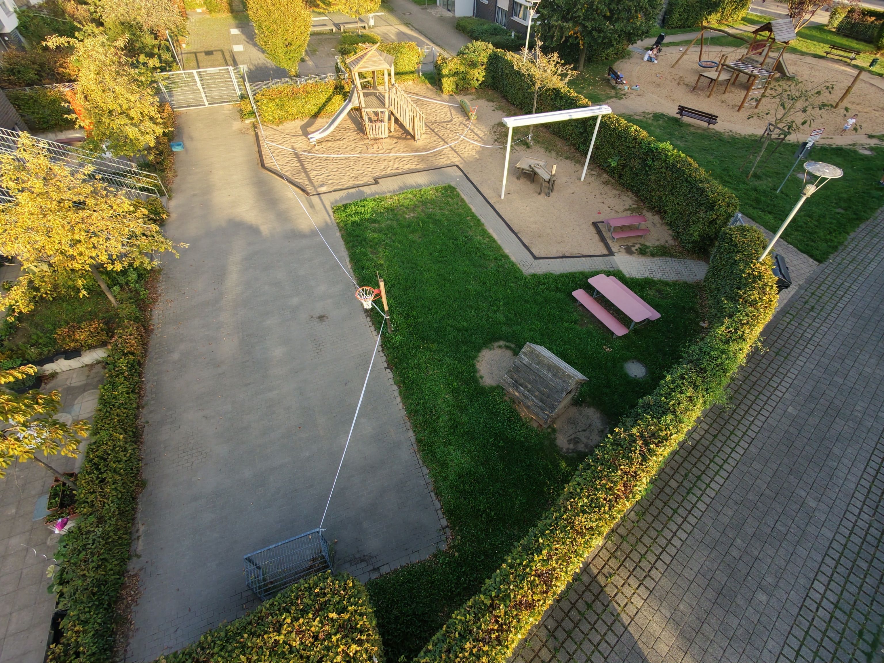 Eine Luftaufnahme zeigt einen von Hecken umgebenen Spielplatz mit Sandflächen, Spielgeräten, Sitzgelegenheiten und Absperrband.