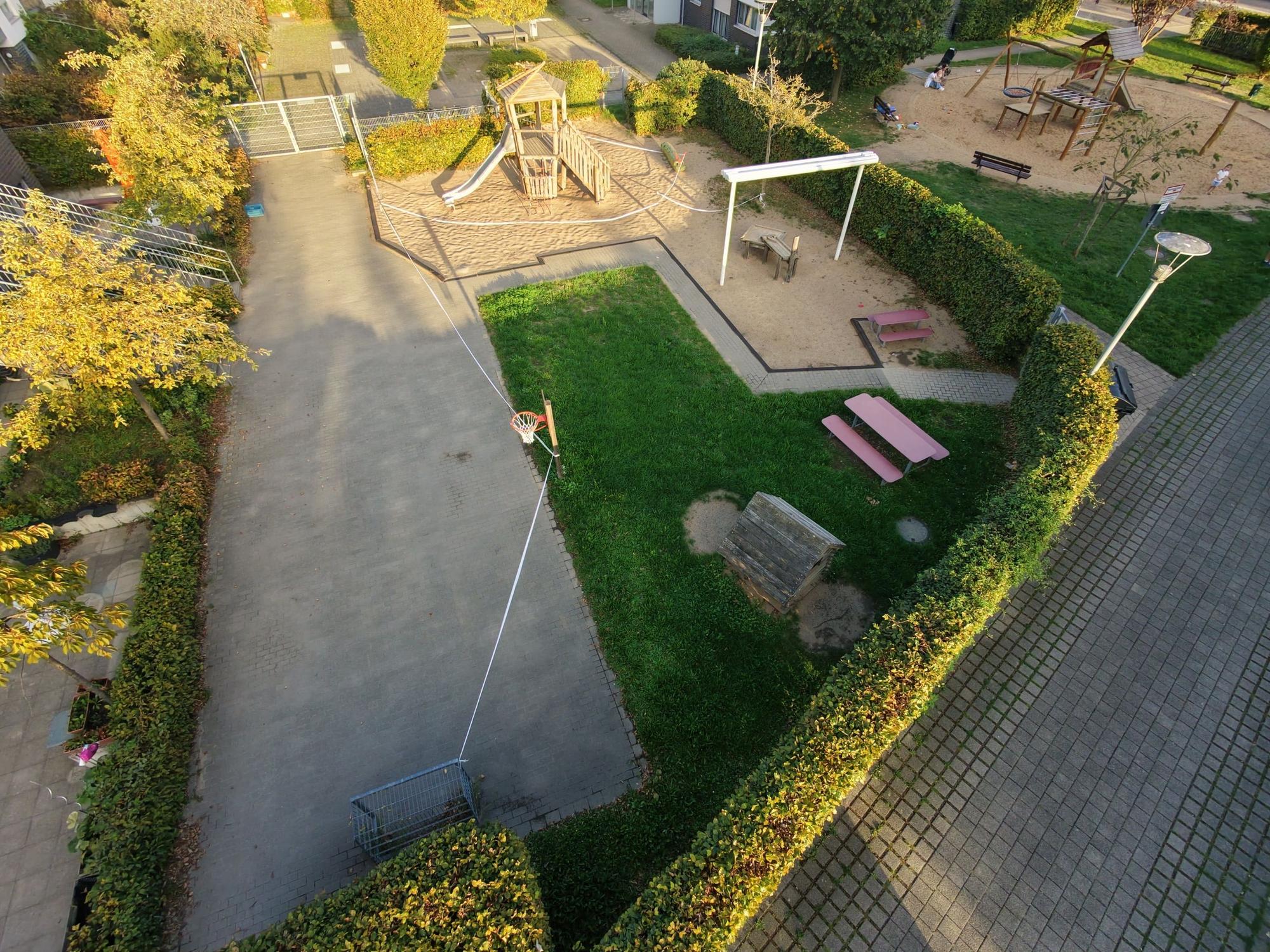 Eine Luftaufnahme zeigt einen von Hecken umgebenen Spielplatz mit Sandflächen, Spielgeräten, Sitzgelegenheiten und Absperrband.