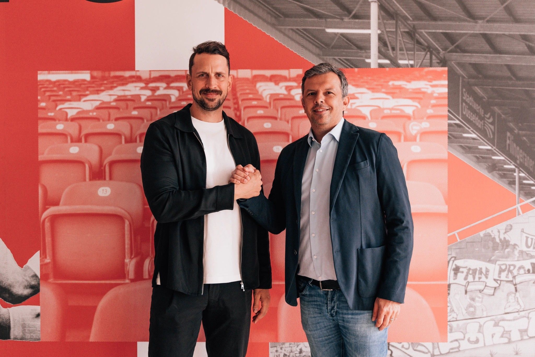 Patrick Fabian und Samir Arabi geben sich einen Handschlag und schauen in die Kamera.