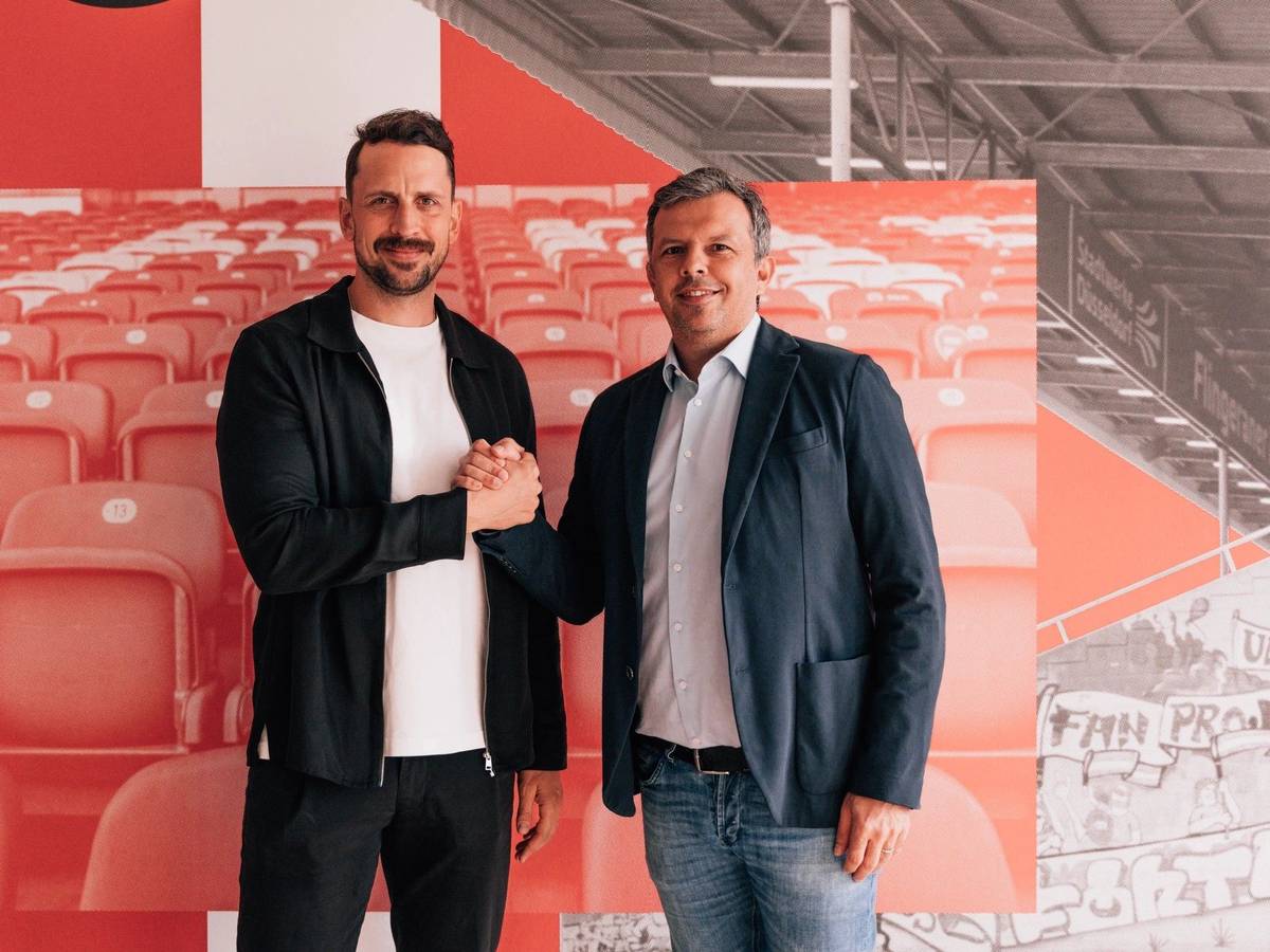 Patrick Fabian und Samir Arabi geben sich einen Handschlag und schauen in die Kamera.