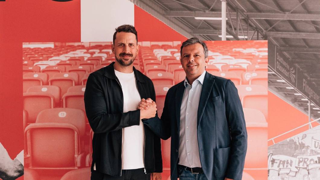 Patrick Fabian und Samir Arabi geben sich einen Handschlag und schauen in die Kamera.
