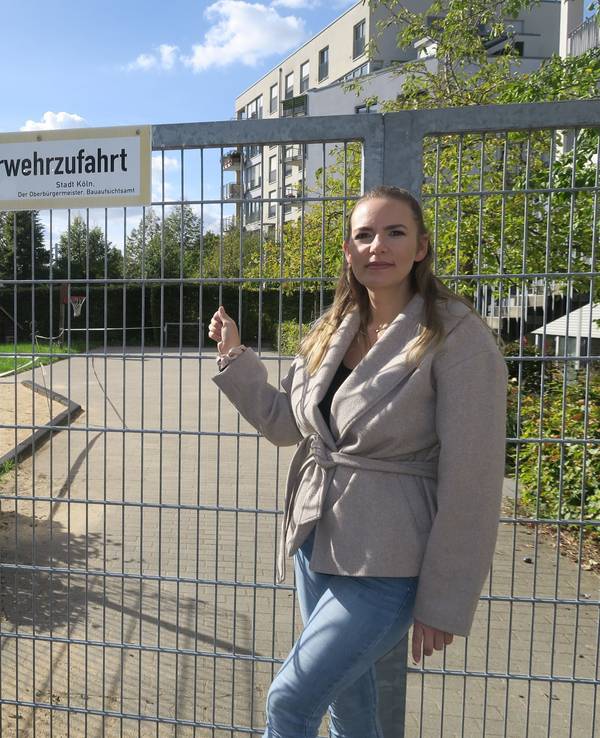 Zwei Frauen stehen vor einem abgesperrten Spielplatz; eine zeigt auf das Tor mit dem Schild „Feuerwehrzufahrt“.