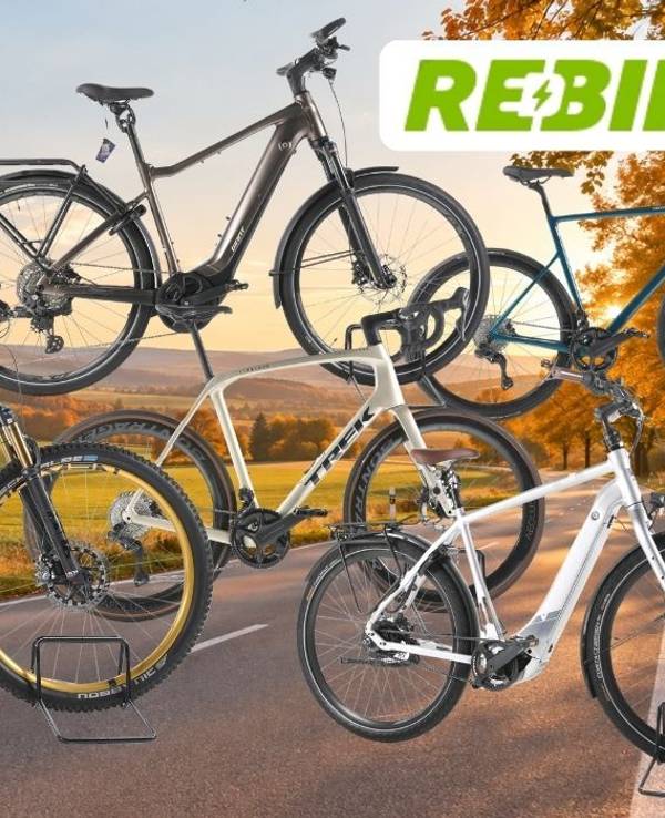 Mehrere refurbished E-Bikes und Fahrräder vor einer herbstlichen Landschaft mit Feldern, Wald und Straße; oben rechts steht das Rebike-Logo.