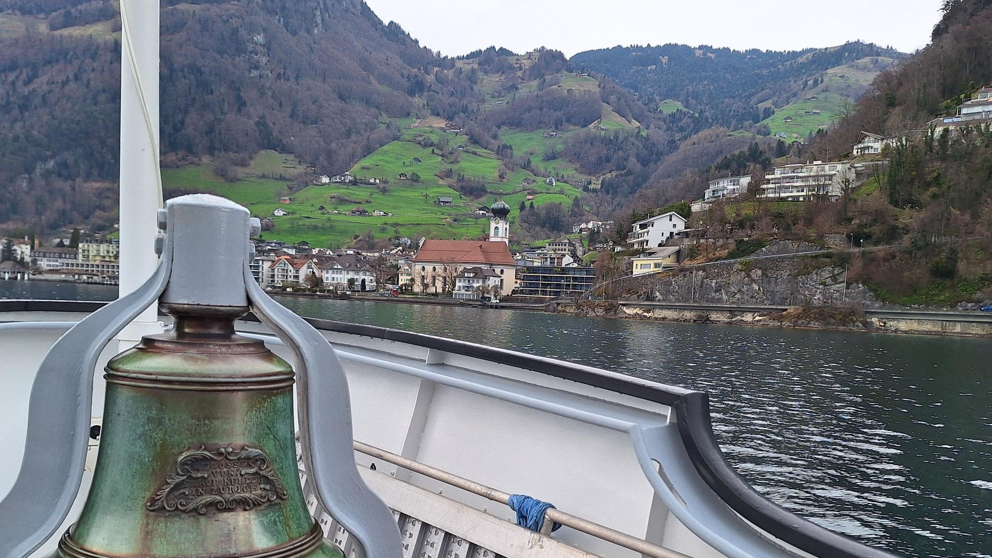 Blick von einem Schiff auf eine grüne Alm mit Kirchturm