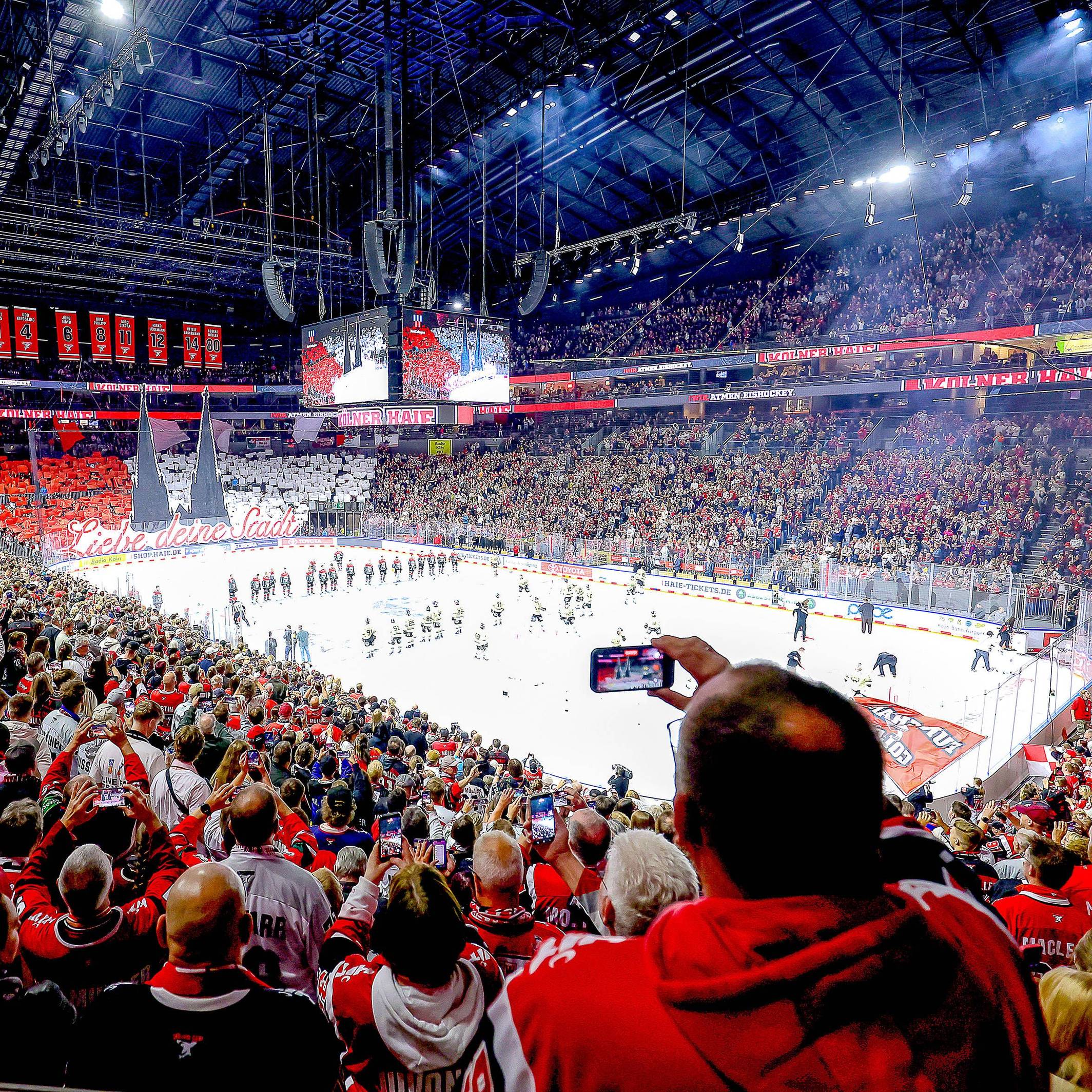 Ein Weitwinkel-Bild aus der vollen Lanxess-Arena, während die Haie-Fans auf der Südtribüne eine rot-weiße Dom-Choreografie zeigen.