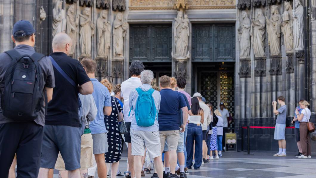 Touristen stehen vor dem Haupteingang des Kölner Doms Schlange.