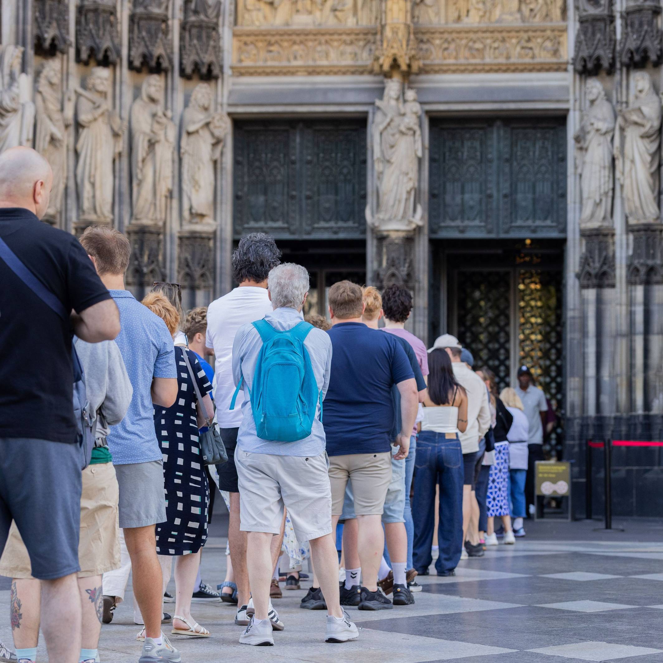 Touristen stehen vor dem Haupteingang des Kölner Doms Schlange.