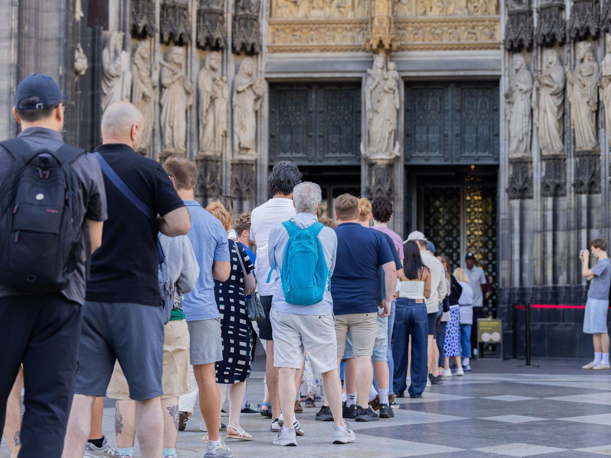 Touristen stehen vor dem Haupteingang des Kölner Doms Schlange.