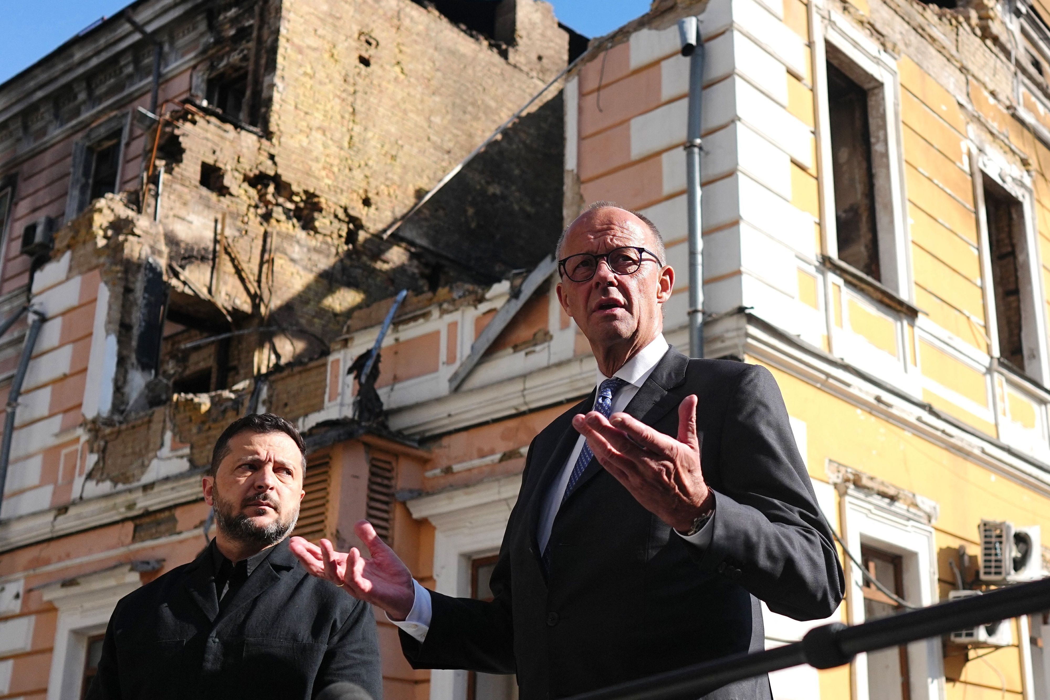 Bundeskanzler Friedrich Merz (r., CDU) und Wolodymyr Selenskyj (l.), Präsident der Ukraine, stehen am zerstörten Gebäude der Nationalen Akademie der Wissenschaften.