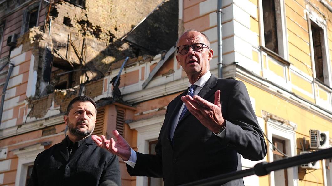 Bundeskanzler Friedrich Merz (r., CDU) und Wolodymyr Selenskyj (l.), Präsident der Ukraine, stehen am zerstörten Gebäude der Nationalen Akademie der Wissenschaften.