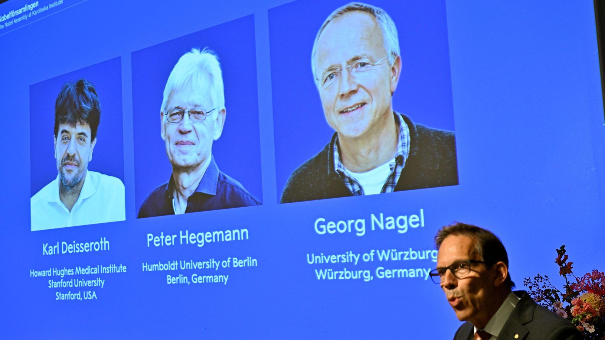 Karl Deisseroth, Peter Hegemann und Georg Nagel sind auf dem Bildschirm zu sehen, als ihnen der Nobelpreis für Physiologie oder Medizin 2026 verliehen wird.
