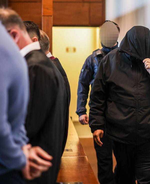 Einer der sieben Angeklagten (r.) wird von einem Justizbeamten in den Gerichtssaal gebracht.