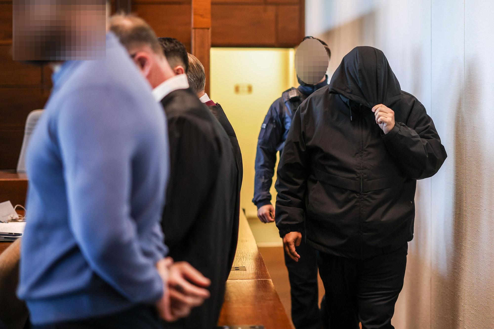 Einer der sieben Angeklagten (r.) wird von einem Justizbeamten in den Gerichtssaal gebracht.