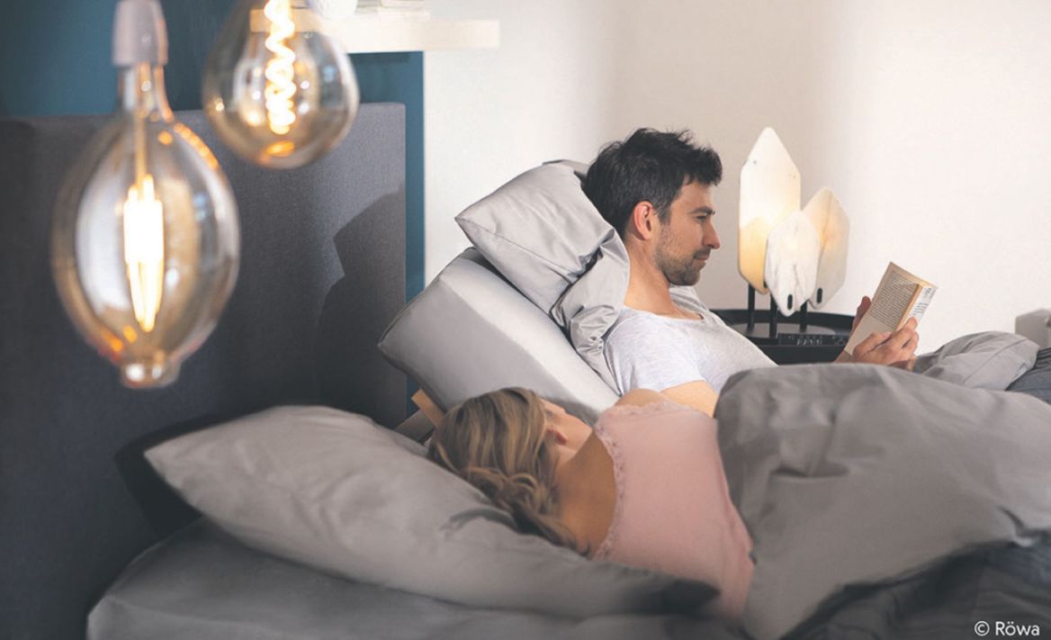 Paar abends im Bett – der Mann liest in aufrecht sitzender Position