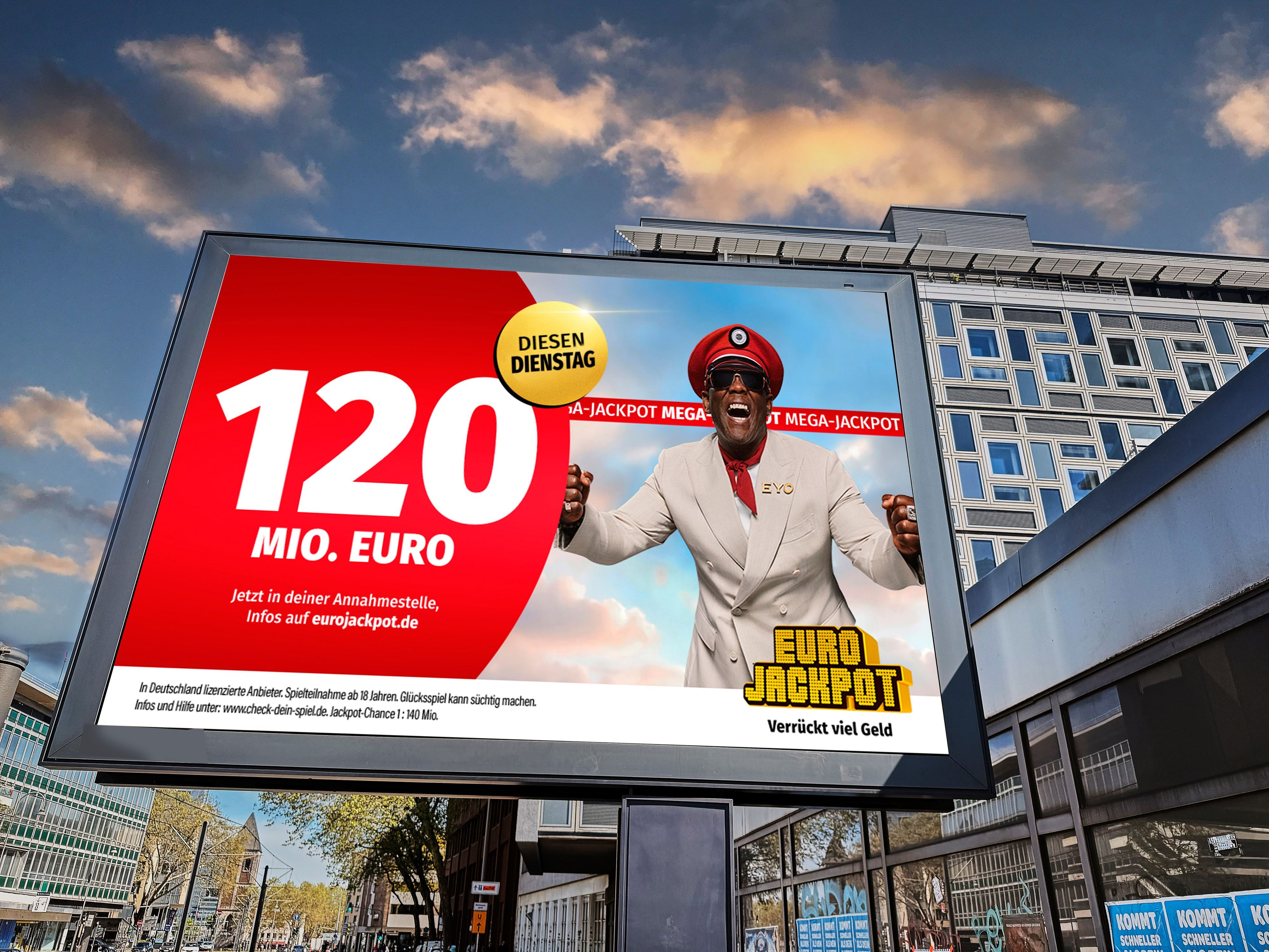 Eurojackpot-Kampagnenplakat auf einer Stadtlichttafel: roter Kreis mit „120 Mio. Euro“ und jubelnder Mann in roter Kapitänsmütze, rechts das Logo „Euro Jackpot – Verrückt viel Geld“.
