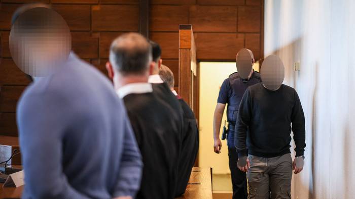 Ein Angeklagter (r) wird von einem Justizbeamten in den Gerichtssaal gebracht. Der Raubüberfall in einer Hürther Lagerhalle gilt als Auslöser einer massiven Gewaltspirale, die als „Kölner Drogenkrieg“ bekannt wurde und im Sommer 2024 Köln und die Region in Atem hielt.
