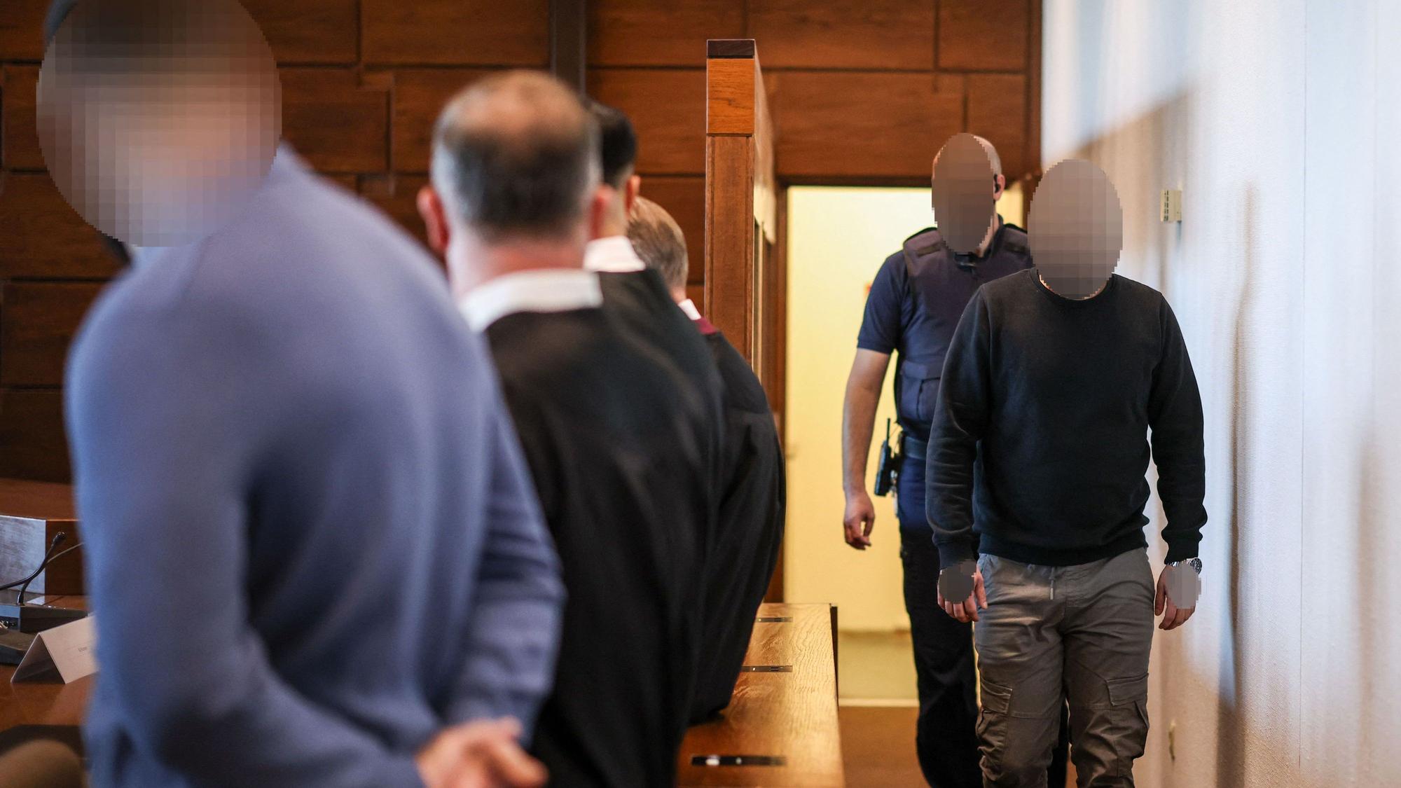 Ein Angeklagter (r) wird von einem Justizbeamten in den Gerichtssaal gebracht. Der Raubüberfall in einer Hürther Lagerhalle gilt als Auslöser einer massiven Gewaltspirale, die als „Kölner Drogenkrieg“ bekannt wurde und im Sommer 2024 Köln und die Region in Atem hielt.