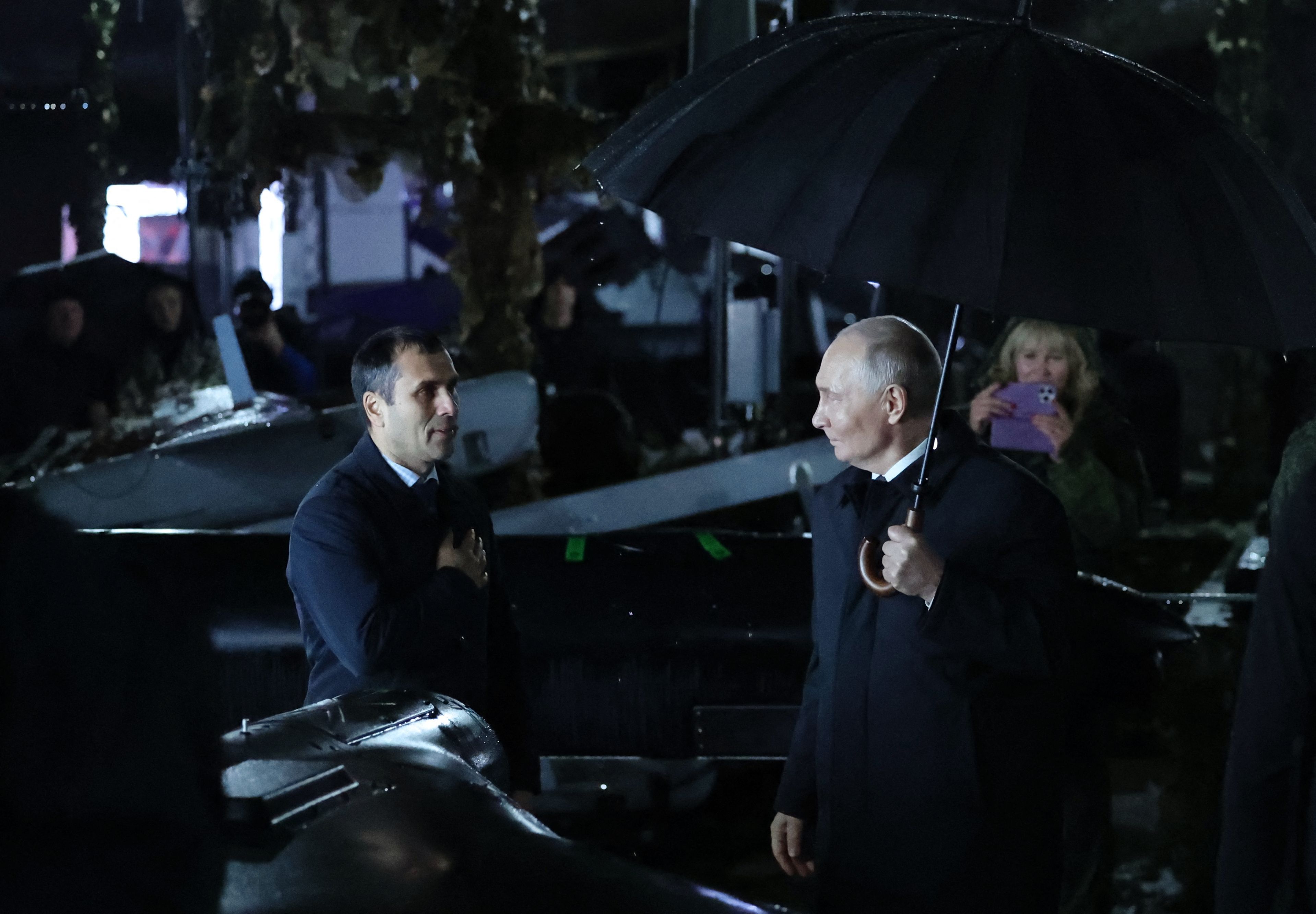 Der russische Präsident Wladimir Putin (rechts) hält einen Regenschirm in der Hand, während er am 2. Oktober 2026 bei einem Besuch eines Truppenübungsplatzes in der Region Tscheljabinsk im Regen steht.
