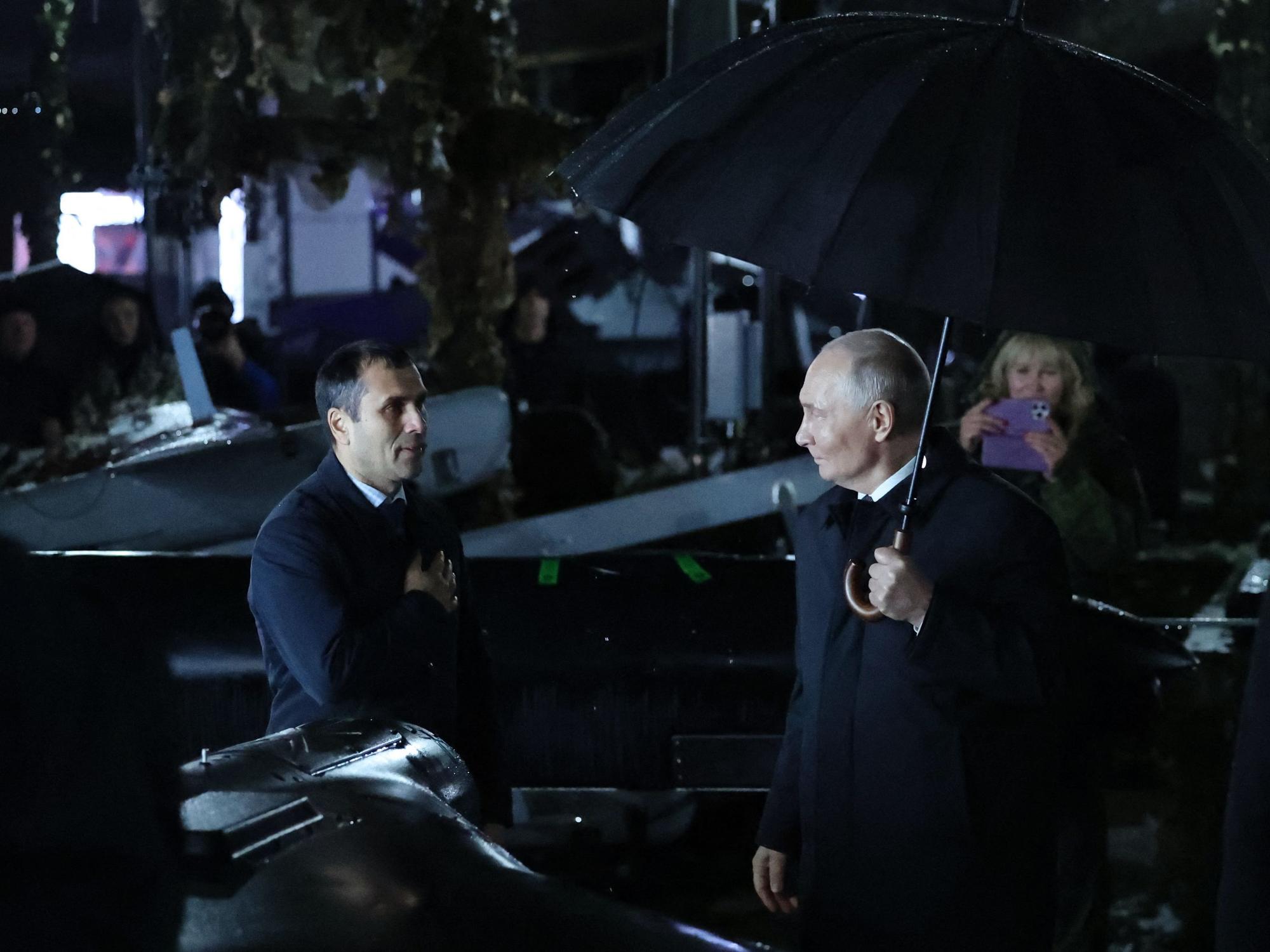 Der russische Präsident Wladimir Putin (rechts) hält einen Regenschirm in der Hand, während er am 2. Oktober 2026 bei einem Besuch eines Truppenübungsplatzes in der Region Tscheljabinsk im Regen steht.