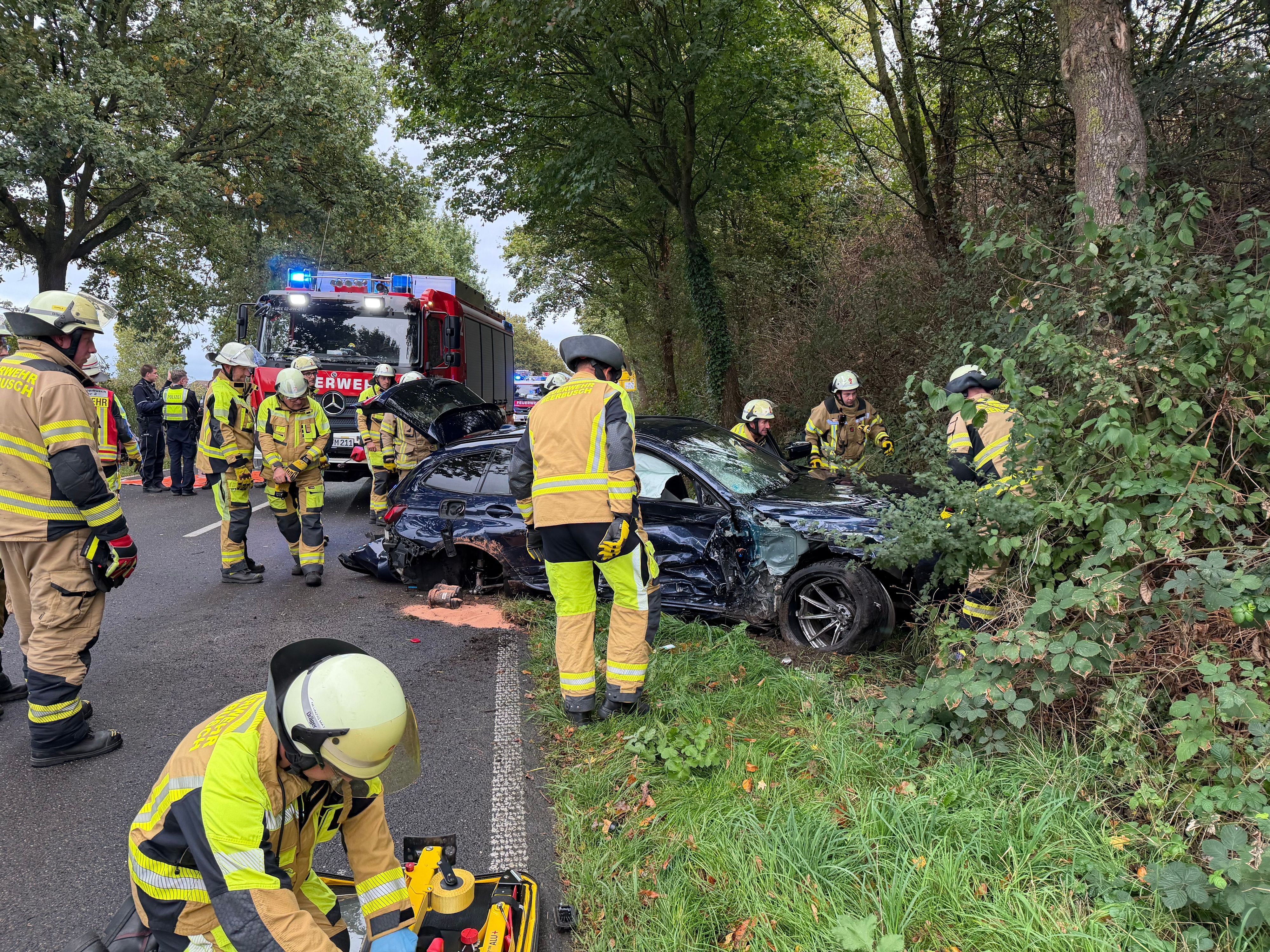 Einsatzkräfte der Feuerwehr sind an einem stark deformierten Auto im Einsatz. Der Wagen war infolge eines Unfalls seitlich gegen einen Baum geprallt.