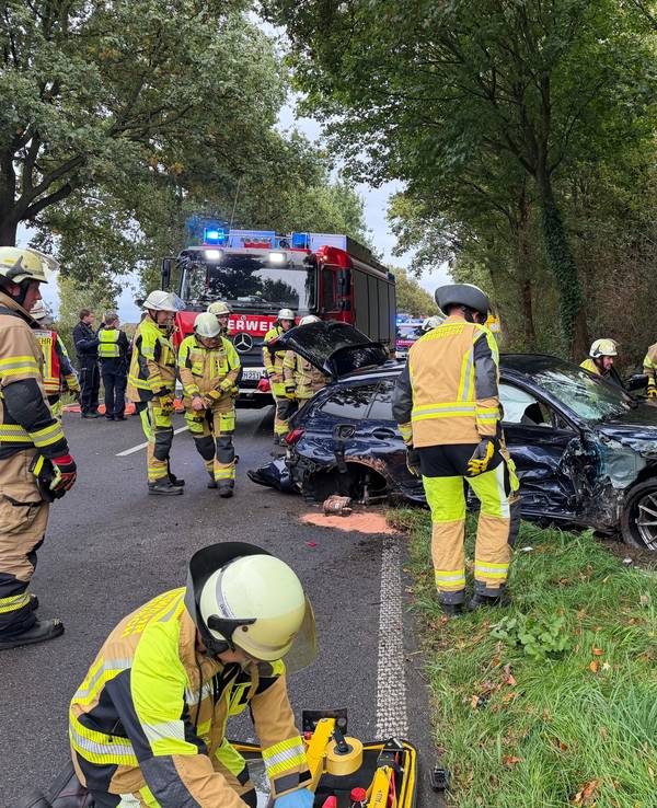 Einsatzkräfte der Feuerwehr sind an einem stark deformierten Auto im Einsatz. Der Wagen war infolge eines Unfalls seitlich gegen einen Baum geprallt.
