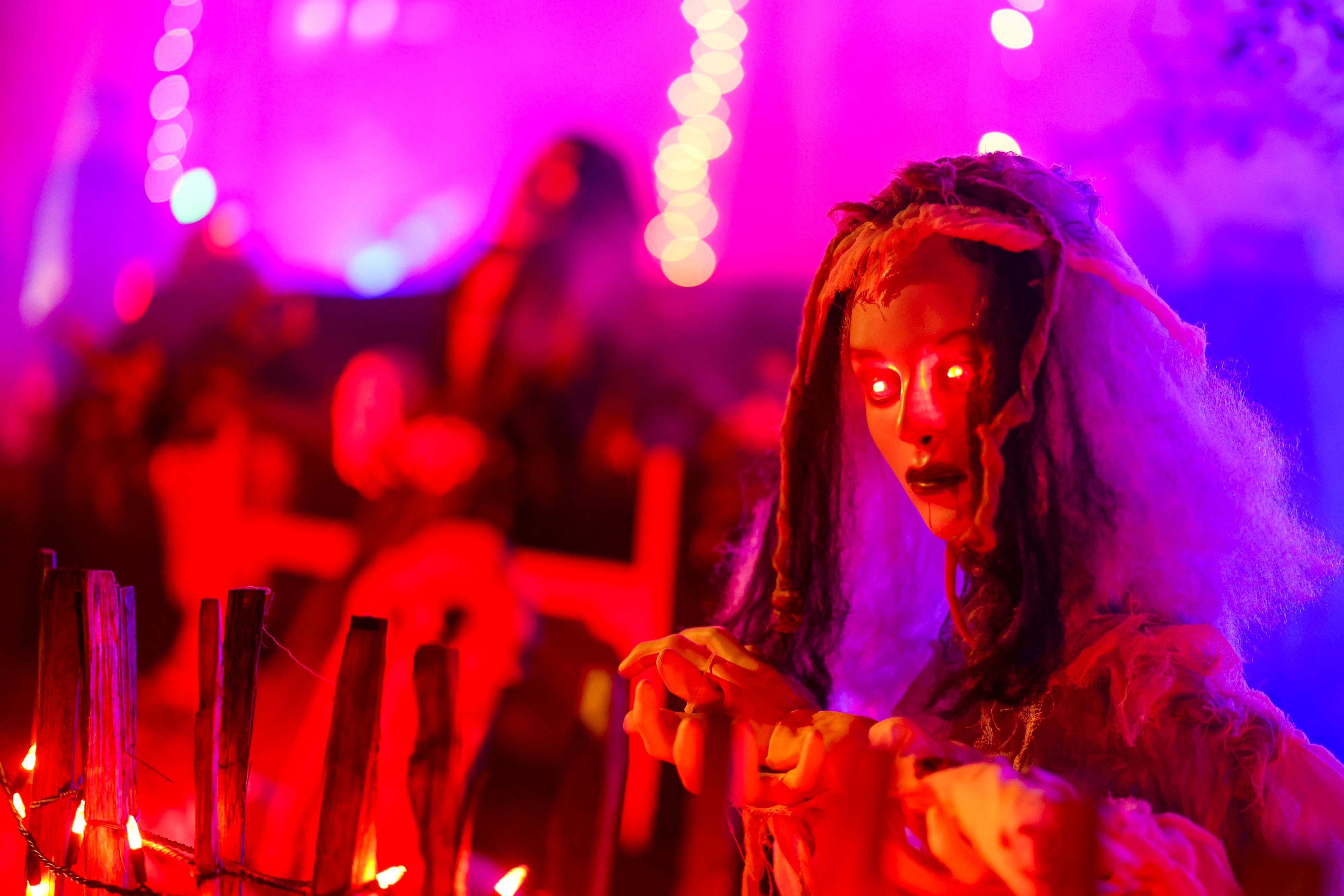 An einem Zaun wartet eine gruselige Figur mit rot leuchtenden Augen auf die Besucher im Halloween-Grusel-Haus..