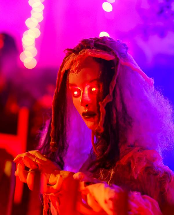 An einem Zaun wartet eine gruselige Figur mit rot leuchtenden Augen auf die Besucher im Halloween-Grusel-Haus..