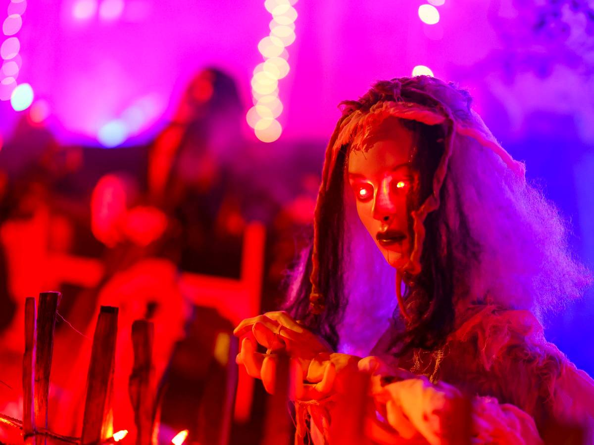 An einem Zaun wartet eine gruselige Figur mit rot leuchtenden Augen auf die Besucher im Halloween-Grusel-Haus..