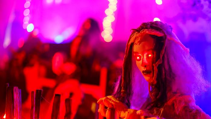 An einem Zaun wartet eine gruselige Figur mit rot leuchtenden Augen auf die Besucher im Halloween-Grusel-Haus..