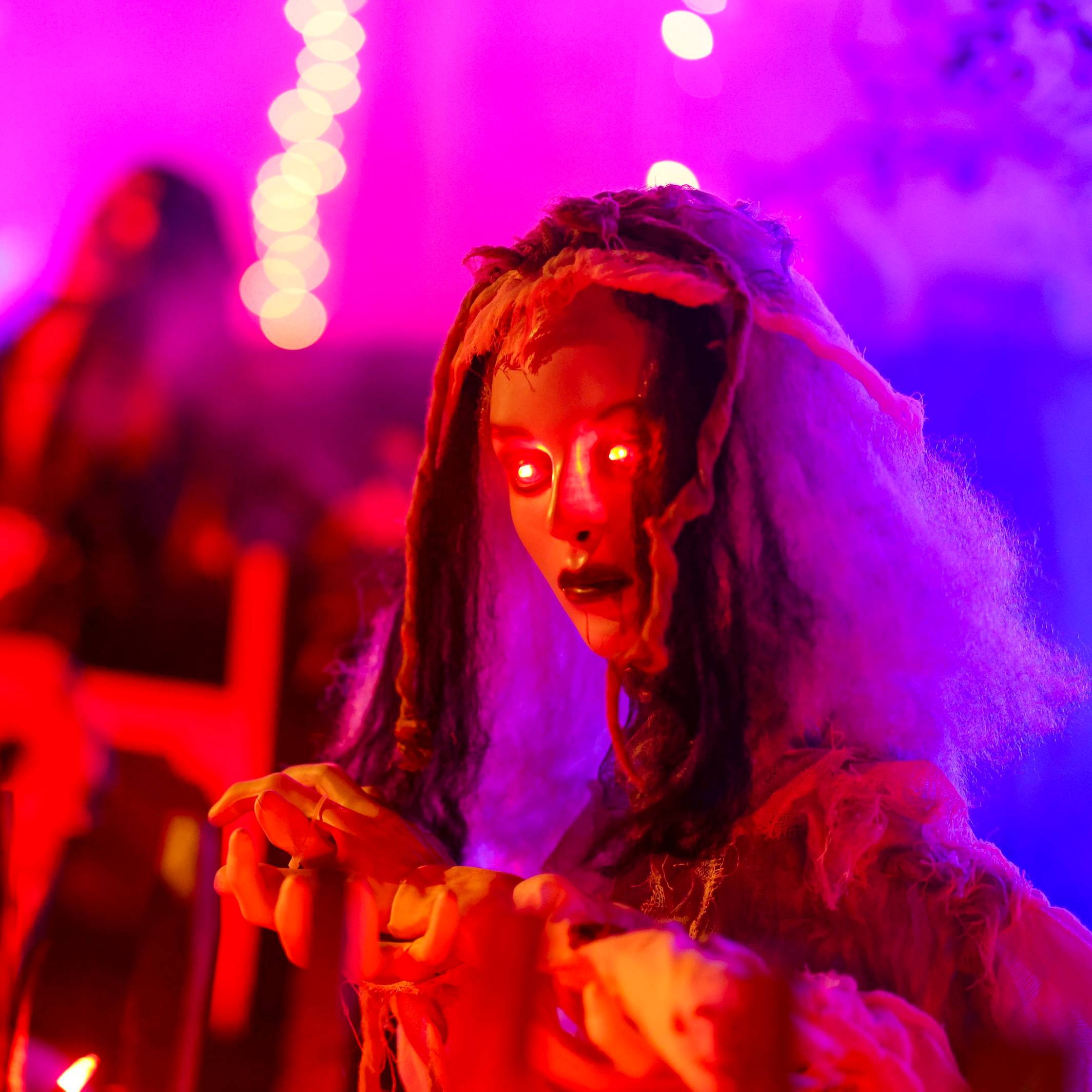 An einem Zaun wartet eine gruselige Figur mit rot leuchtenden Augen auf die Besucher im Halloween-Grusel-Haus.