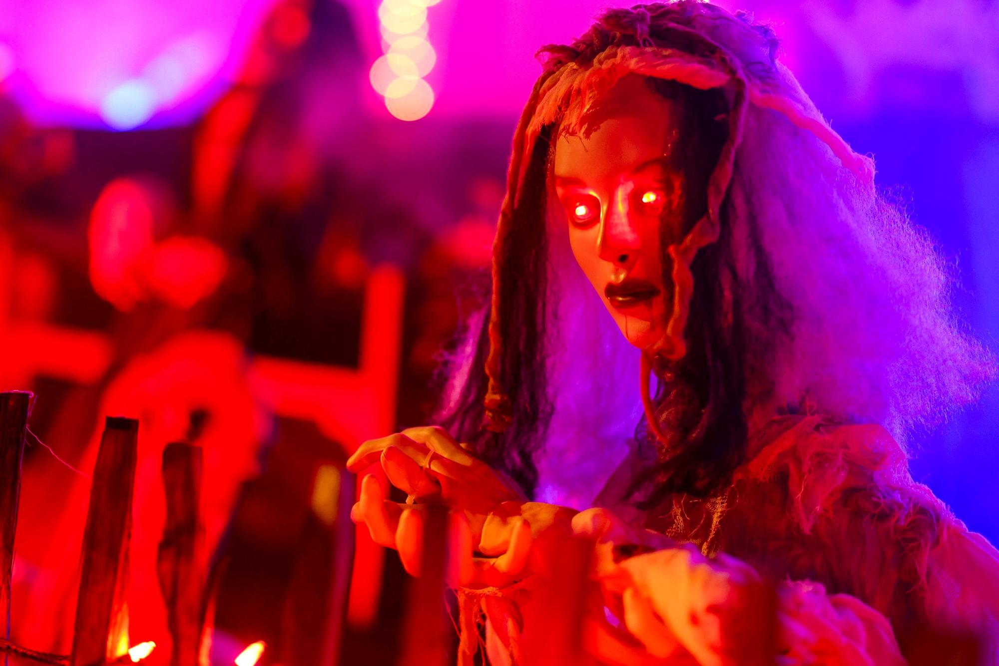 An einem Zaun wartet eine gruselige Figur mit rot leuchtenden Augen auf die Besucher im Halloween-Grusel-Haus..