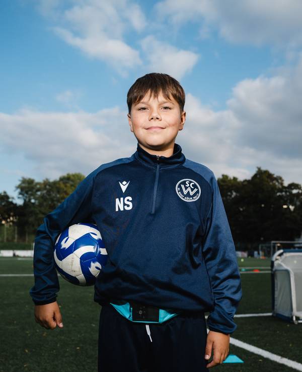 Nick (11) steht auf dem Fußballplatz und hat sich einen Fußball unter den rechten Arm geklemmt.
