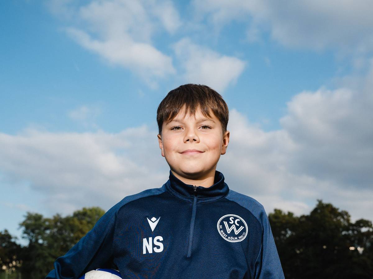 Nick (11) steht auf dem Fußballplatz und hat sich einen Fußball unter den rechten Arm geklemmt.