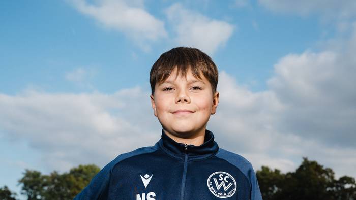 Nick (11) steht auf dem Fußballplatz und hat sich einen Fußball unter den rechten Arm geklemmt.