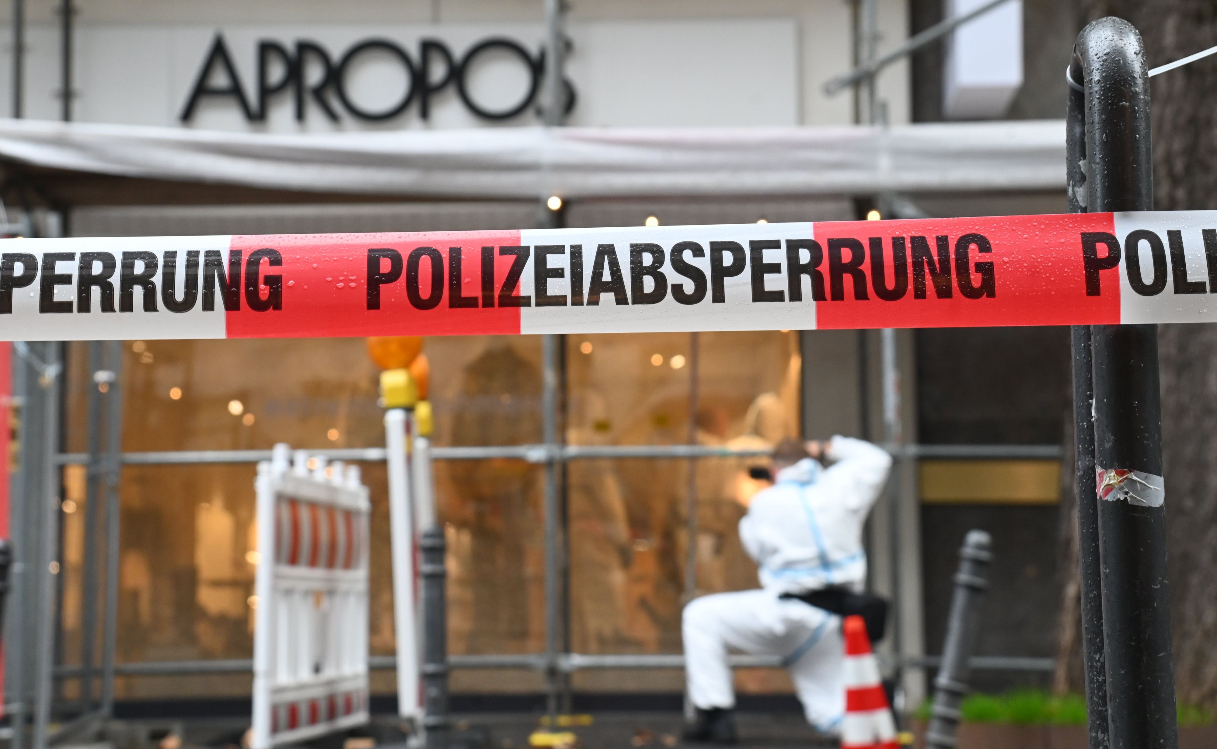 Ein Beamter im Schutzanzug sichert am Modegeschäft Spuren, der Tatort ist von der Polizei mit Flatterband abgesperrt worden.