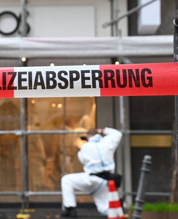 Ein Beamter im Schutzanzug sichert am Modegeschäft Spuren, der Tatort ist von der Polizei mit Flatterband abgesperrt worden.