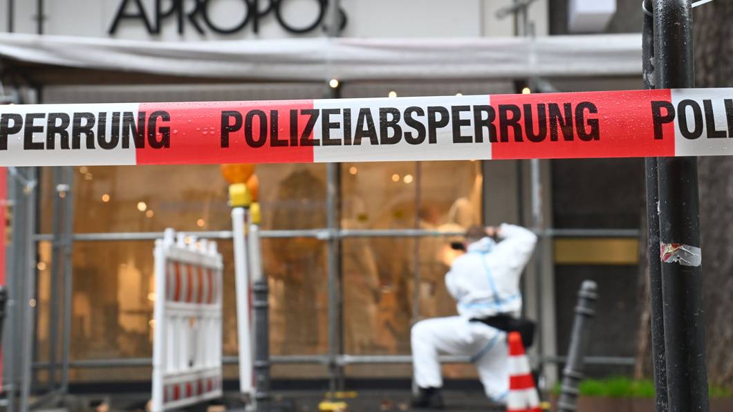 Ein Beamter im Schutzanzug sichert am Modegeschäft Spuren, der Tatort ist von der Polizei mit Flatterband abgesperrt worden.