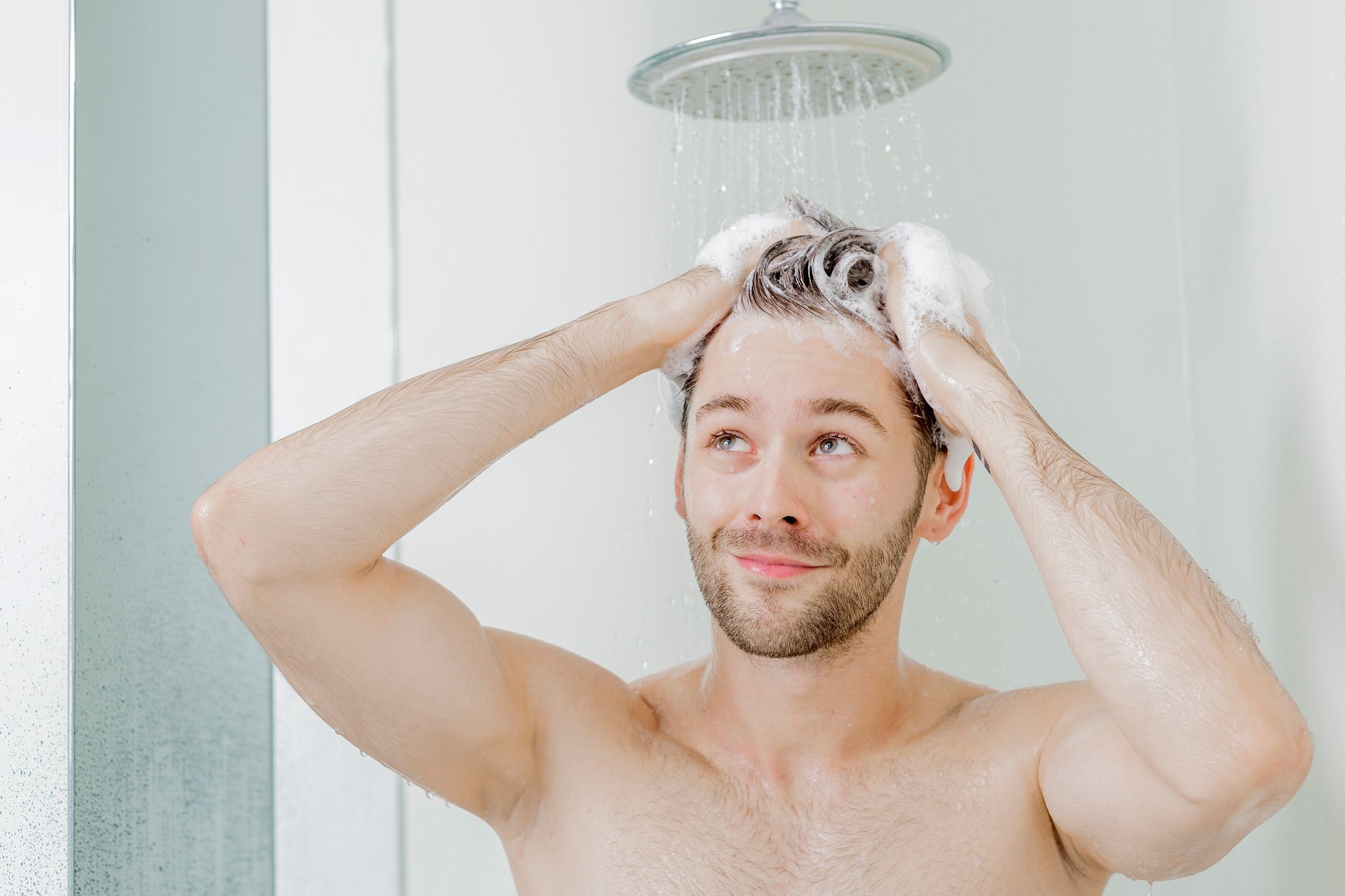 Ein junger Mann wäscht sich die Haare unter der Dusche