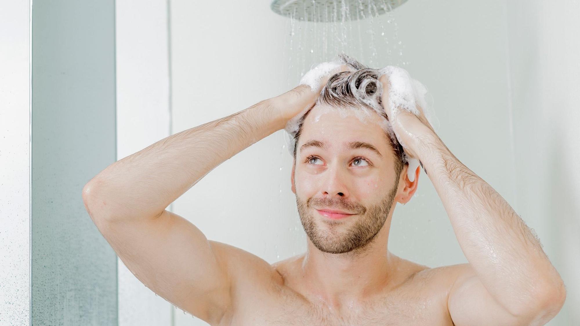 Ein junger Mann wäscht sich die Haare unter der Dusche