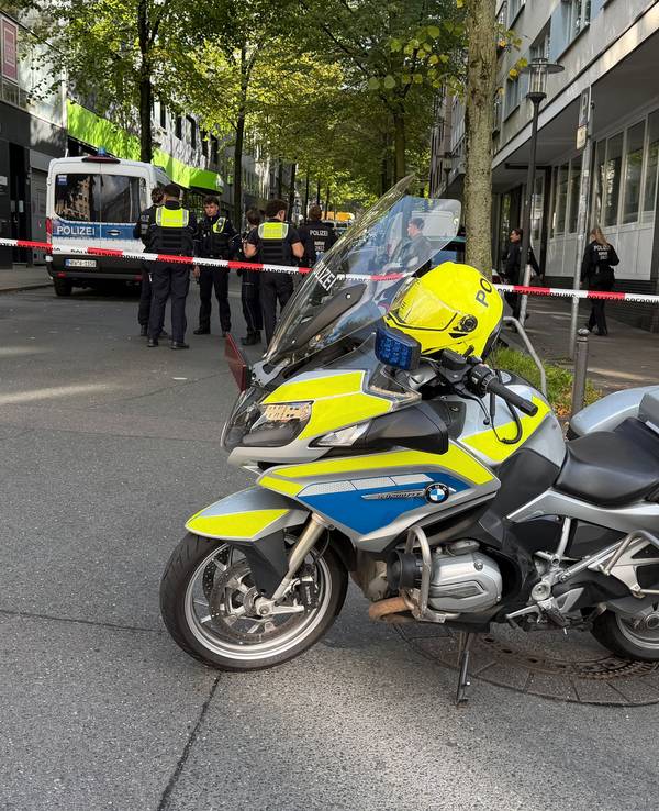 In der Nähe des Tatortes steht ein Polizeimotorrad vor einem Absperrband.