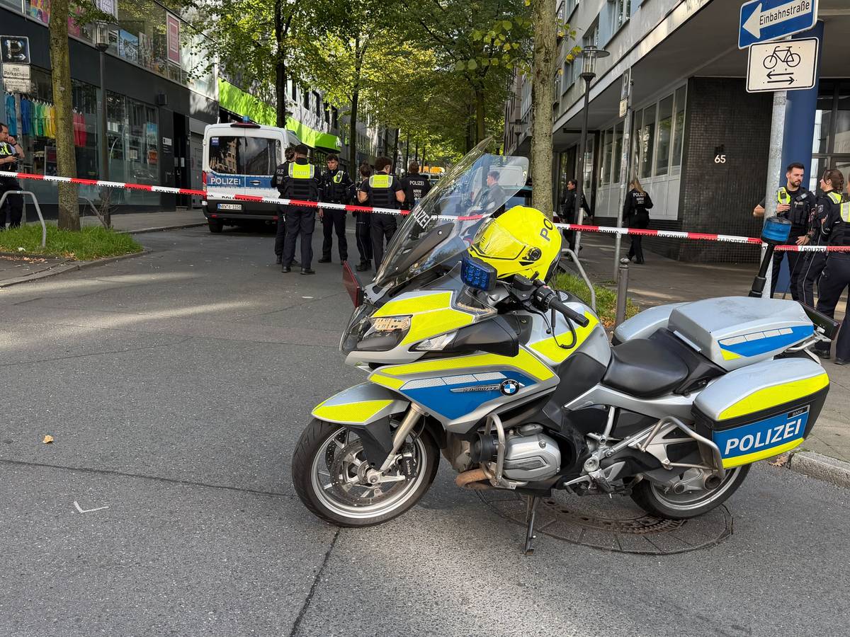 In der Nähe des Tatortes steht ein Polizeimotorrad vor einem Absperrband.