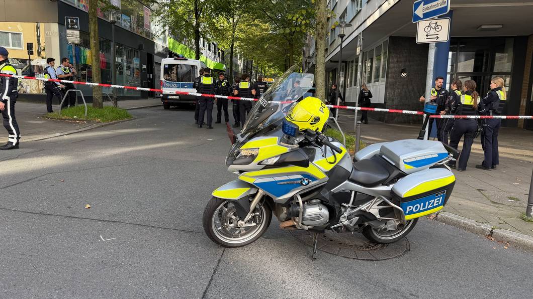 In der Nähe des Tatortes steht ein Polizeimotorrad vor einem Absperrband.