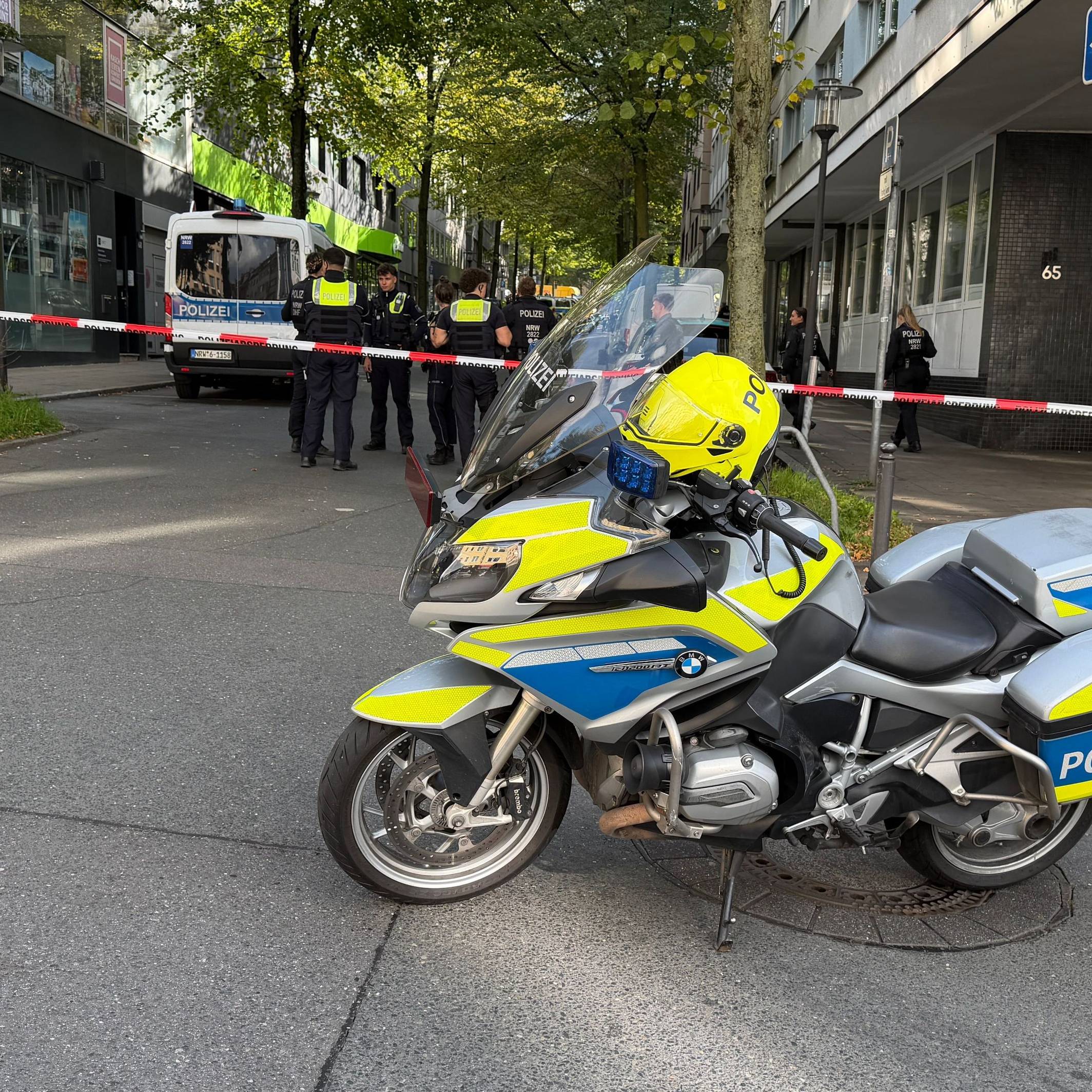 In der Nähe des Tatortes steht ein Polizeimotorrad vor einem Absperrband.