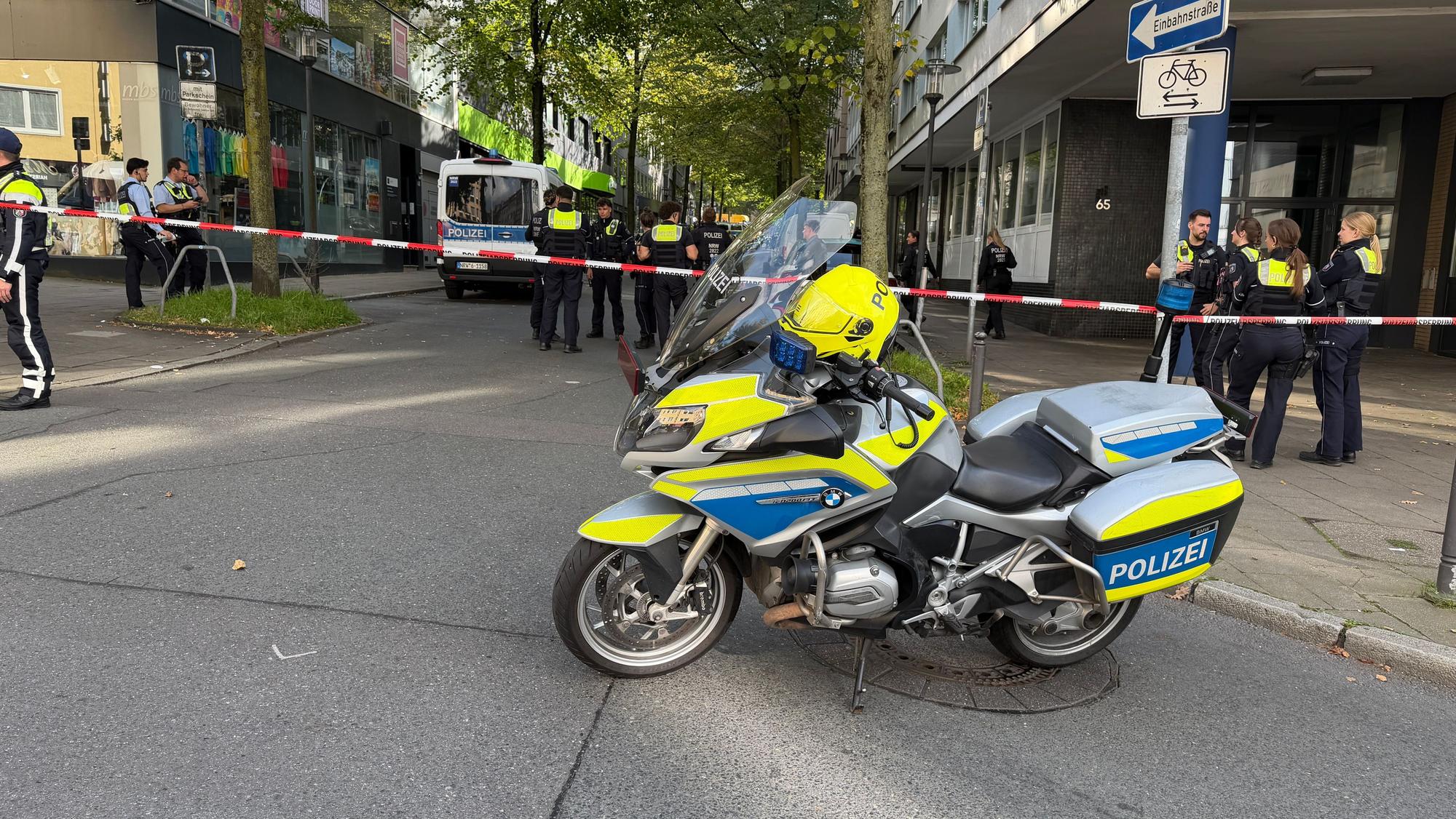 In der Nähe des Tatortes steht ein Polizeimotorrad vor einem Absperrband.