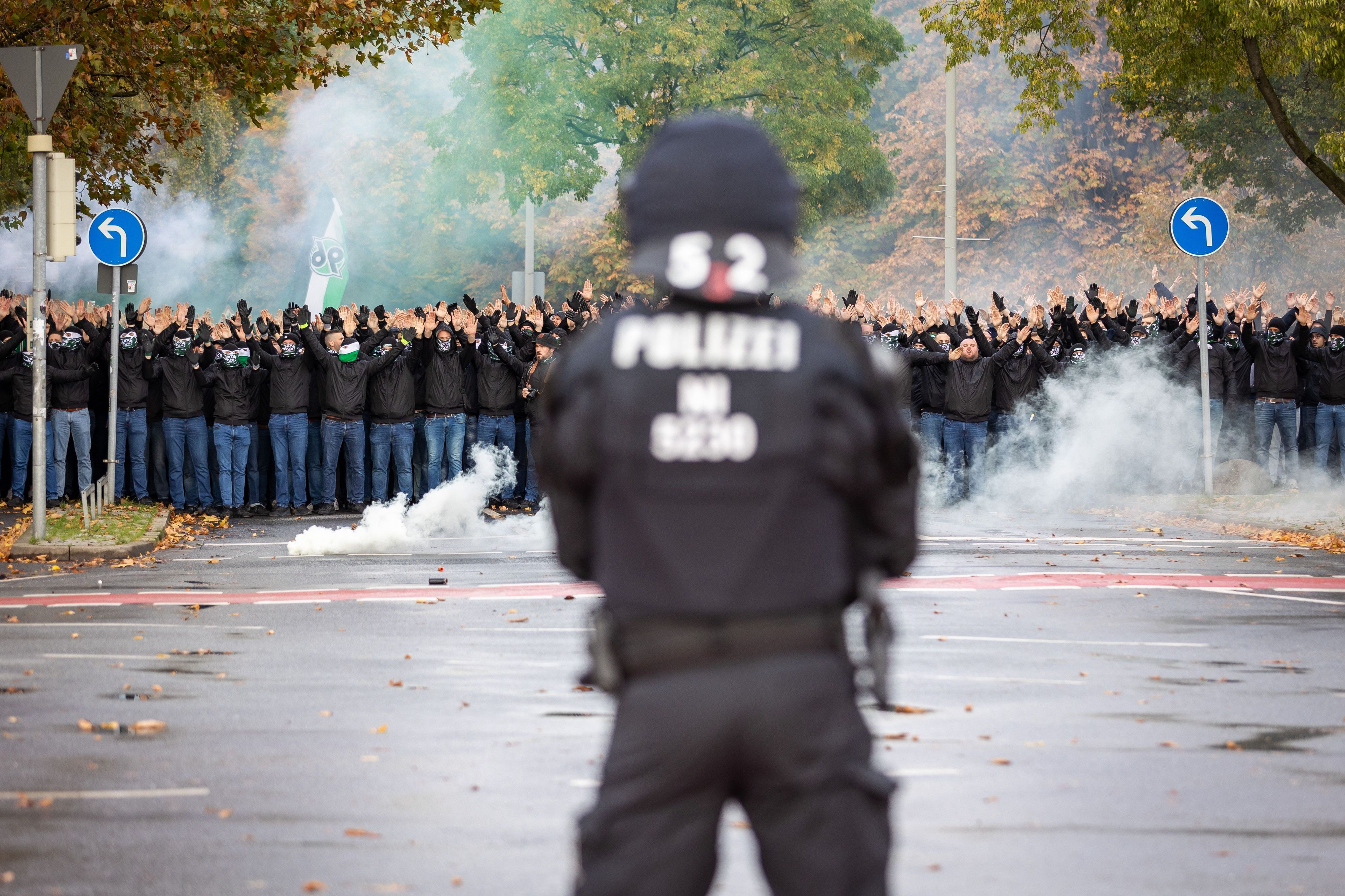 Ein Polizist der vor vielen vermummten Hannover 96 Fans steht.